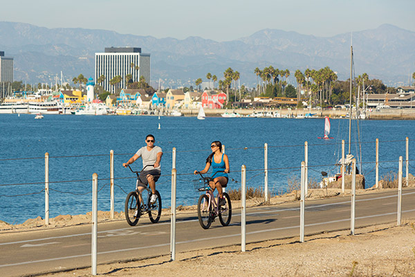 couple riding bikes with boats and mountains in background