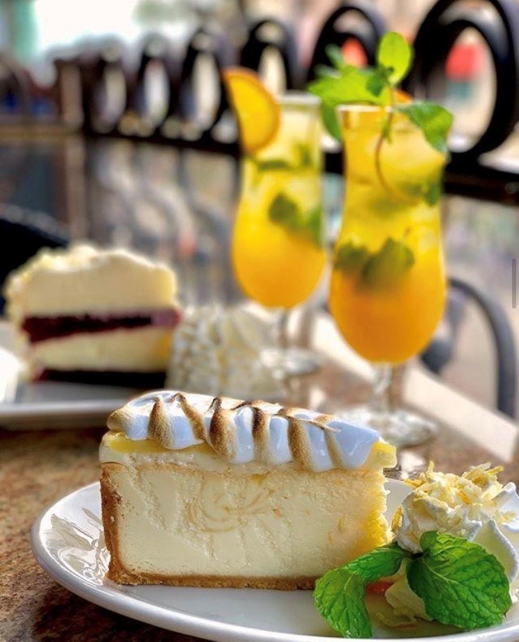 Two slices of cheesecake on an outdoor table with two mimosa drinks