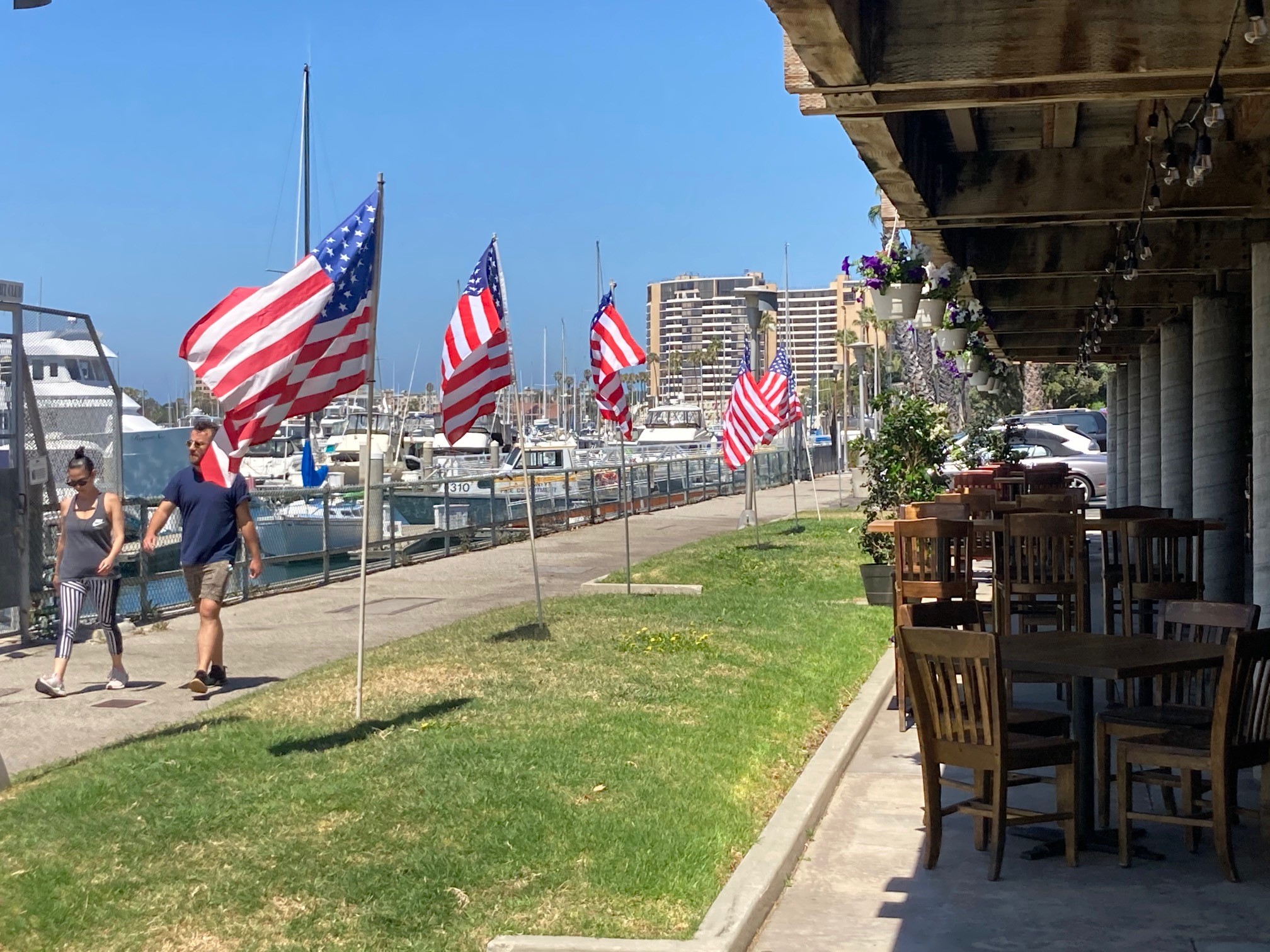 Grass with flags posted along harborfront walk and outdoor restaurant patio seating