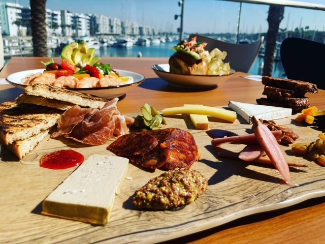 Weekend brunch food including cheese and meat board on table facing harbor and water