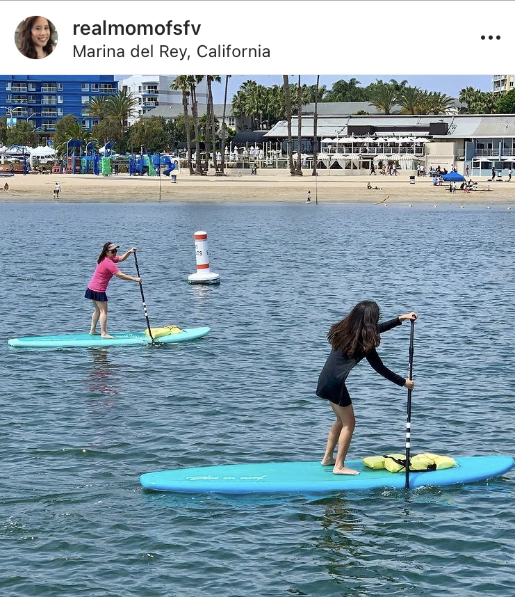 two people on a stand-up paddle board on the ocean by a beach