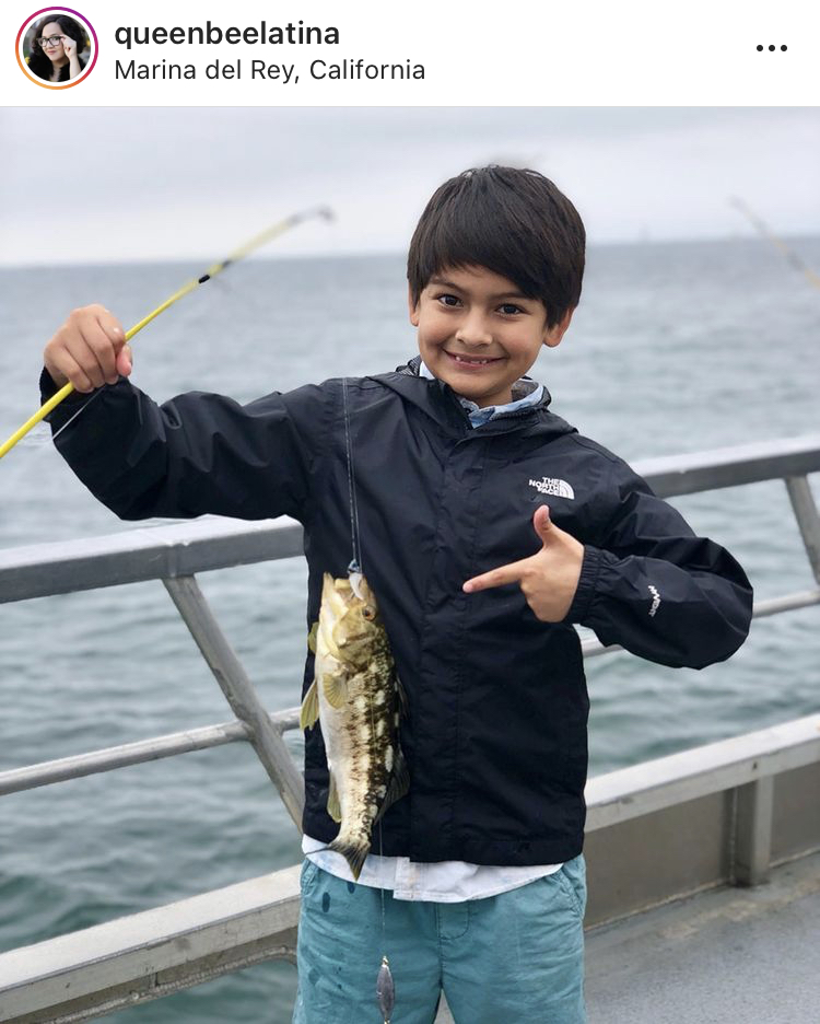 boy holding up fish reeled in from deep-sea fishing trip on a boat in the Pacific Ocean