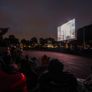 People sitting in lawn chairs and cars watching drive-in movie in Marina del Rey