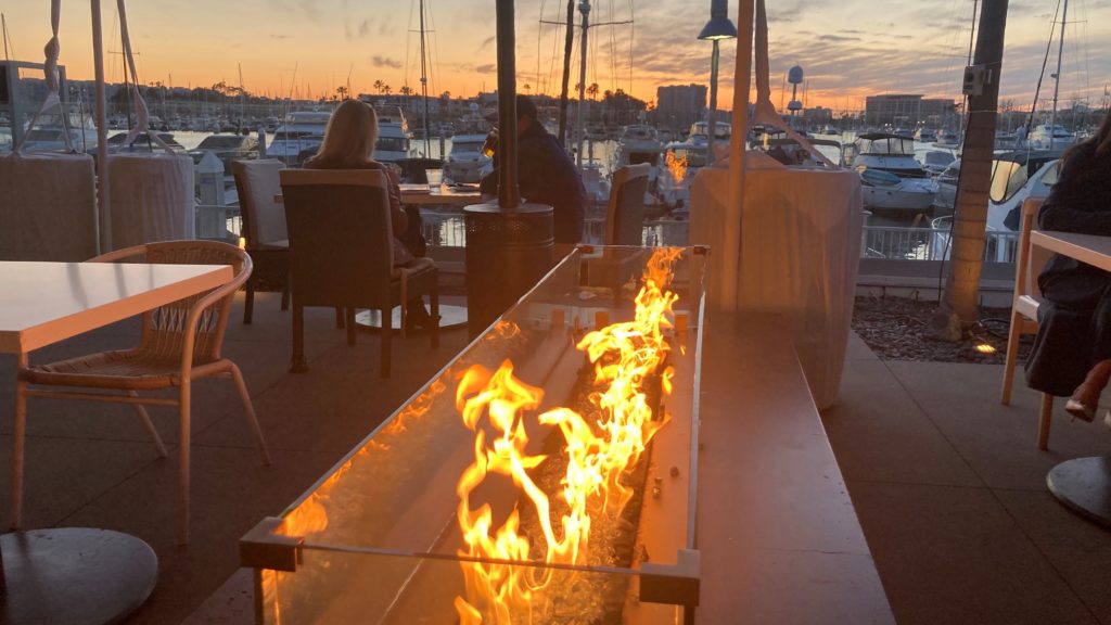 Firepit next to tables at outdoor patio of restaurant with orange sunset sky