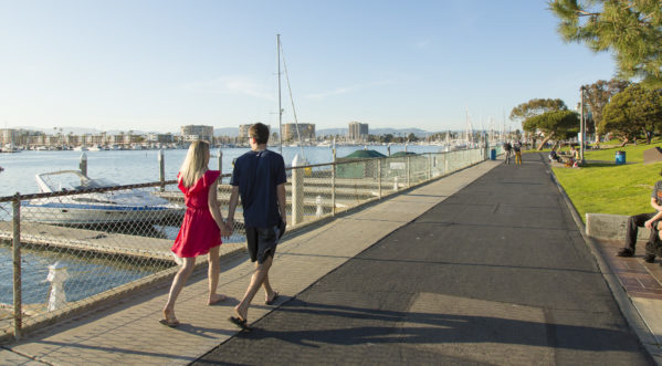 Two people holding hands and walking side by side near the harbor and water at a park