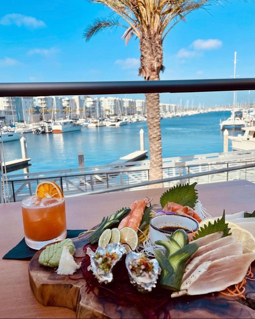 Sashimi platter and drink on table facing harbor and boats