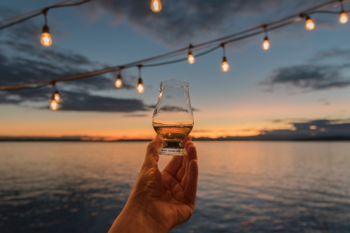 Hand holding shot glass with tequila and sunset with ocean in background