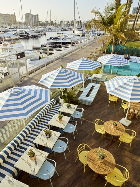 Aerial view of restaurant tables, chairs and umbrellas facing boats in harbor
